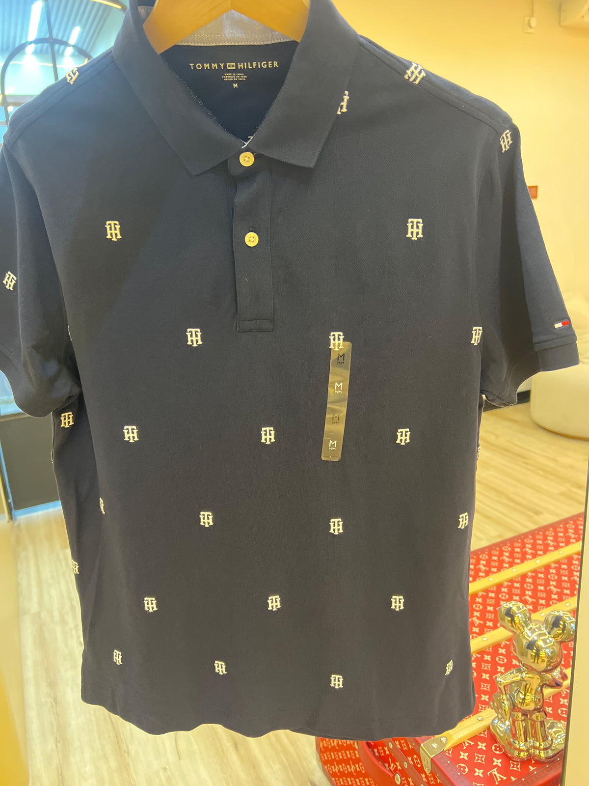 Navy blue Tommy Hilfiger men's polo shirt featuring a small embroidered logo pattern across the fabric