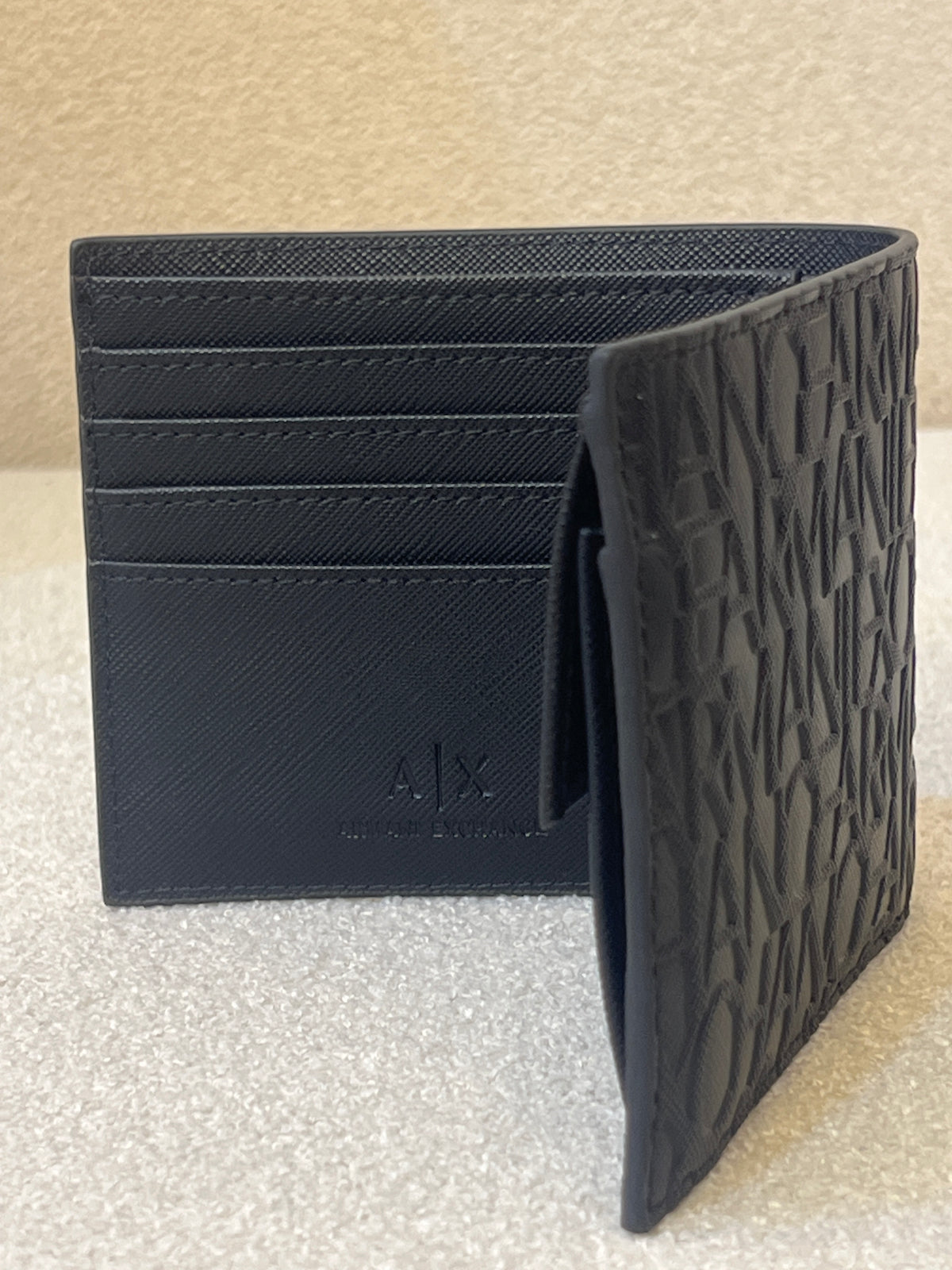 Armani Exchange bifold wallet, likely model 958098_CC838, featuring an all-over embossed logo design in black