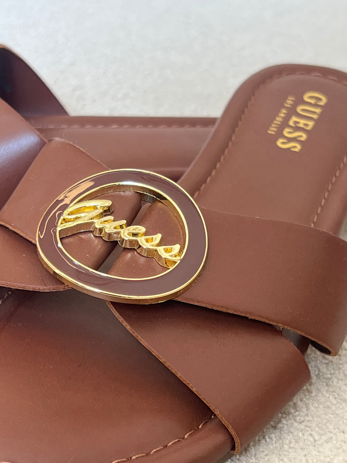 Guess brown slide sandals feature a distinctive gold-toned brand logo on the strap