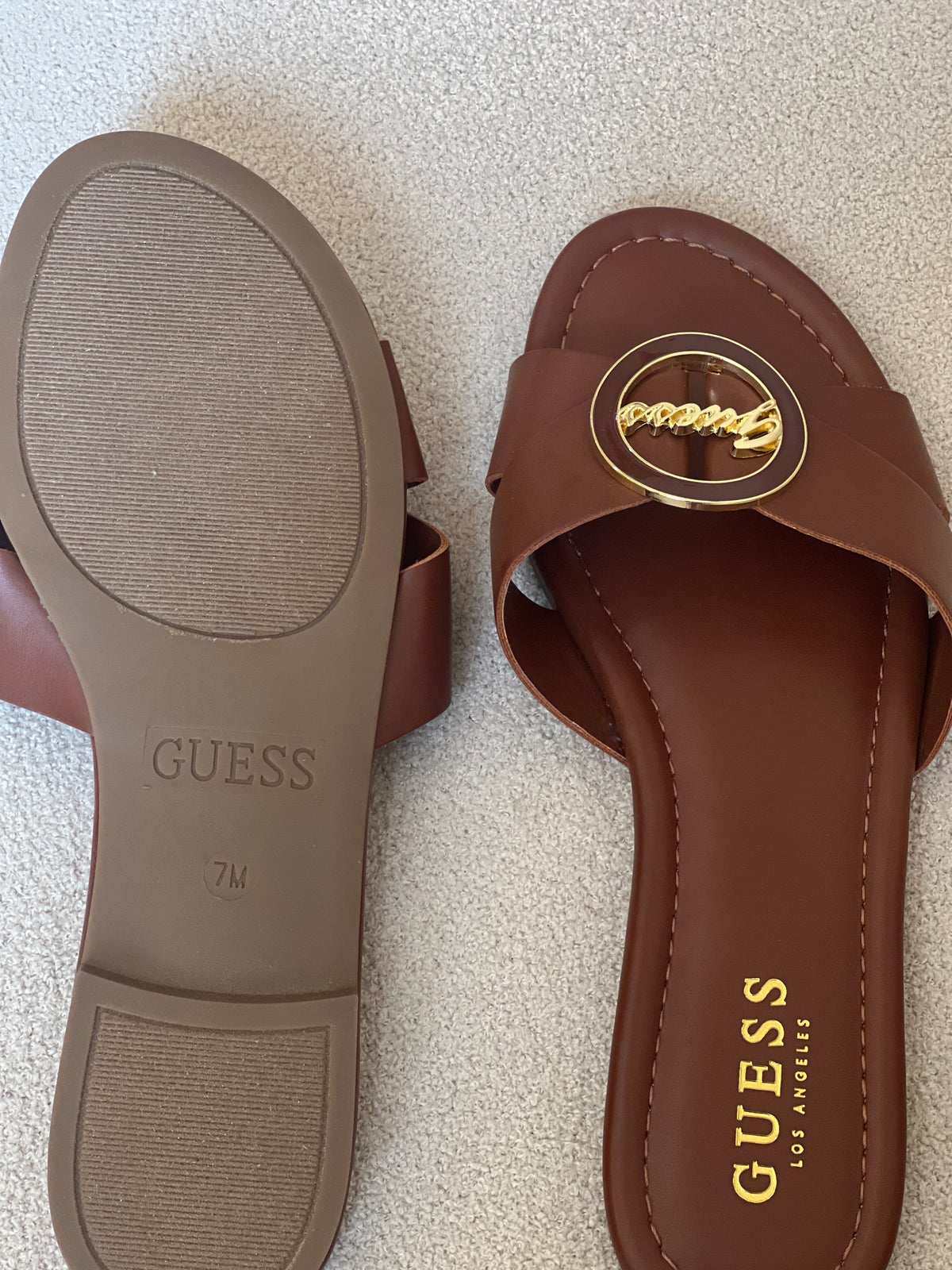 Guess brown slide sandals feature a distinctive gold-toned brand logo on the strap