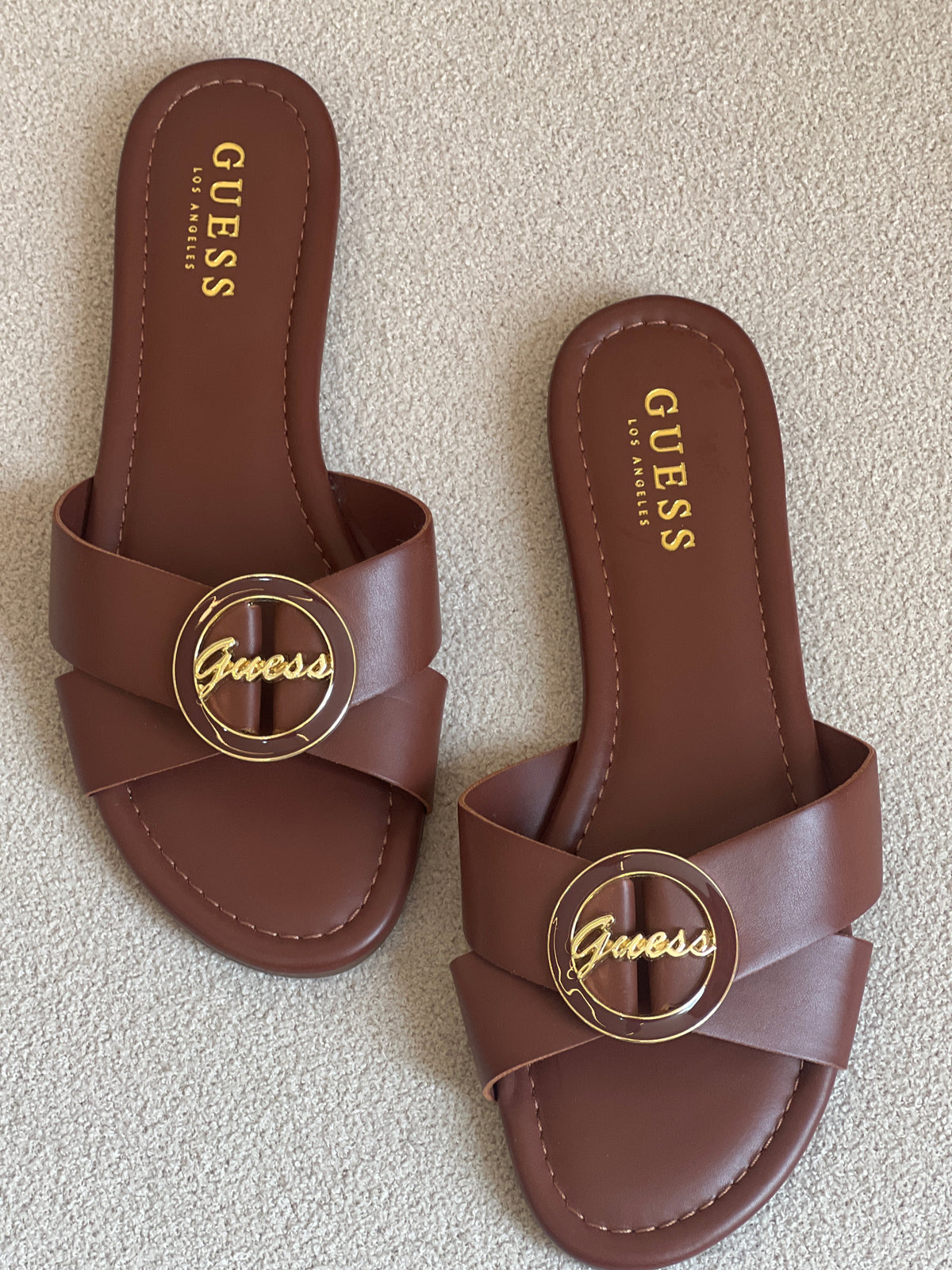 Guess brown slide sandals feature a distinctive gold-toned brand logo on the strap